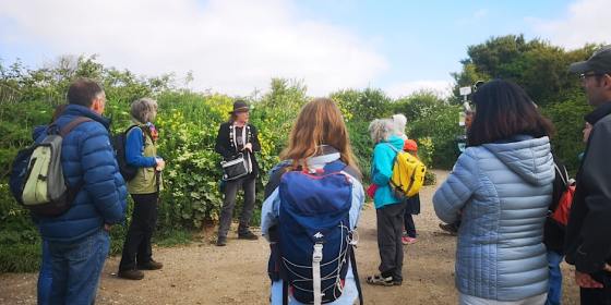 Man talking to a group of people in front of a spring hedgerow