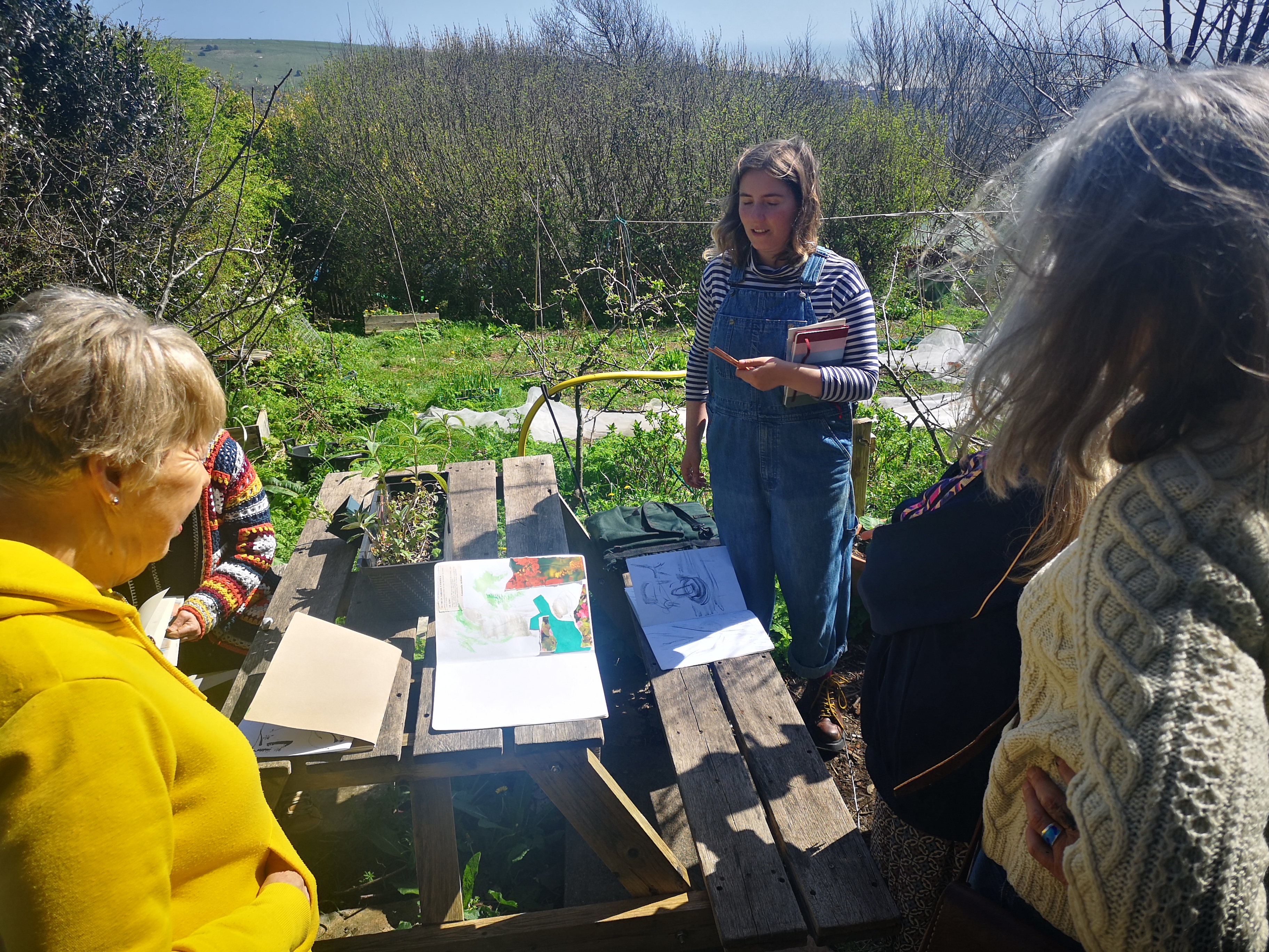 Community artist looking at people's drawings on a picnic table in front of a community garden.
